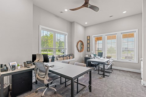 A modern office with a white desk and chairs, a phone, and a fan.