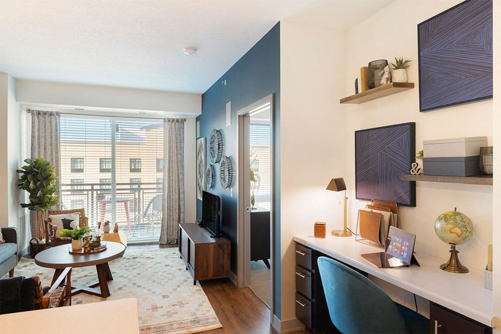 a living room with a desk and a door to a balcony