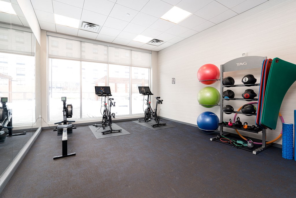 a spacious fitness room with weights and balls and a large window