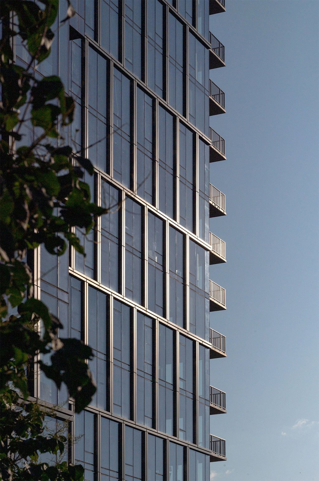 A tall building with many windows and balconies is seen from below.