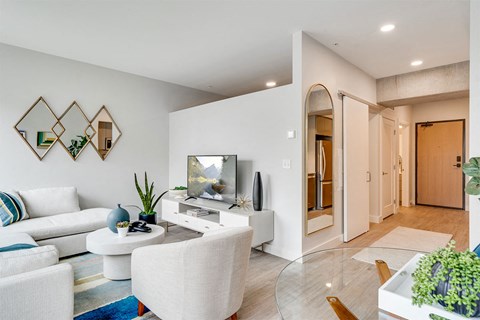 A modern living room with a white sofa, a glass coffee table, and a TV.