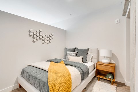 A bedroom with a bed, pillows, a blanket, a nightstand, and a wall decoration.