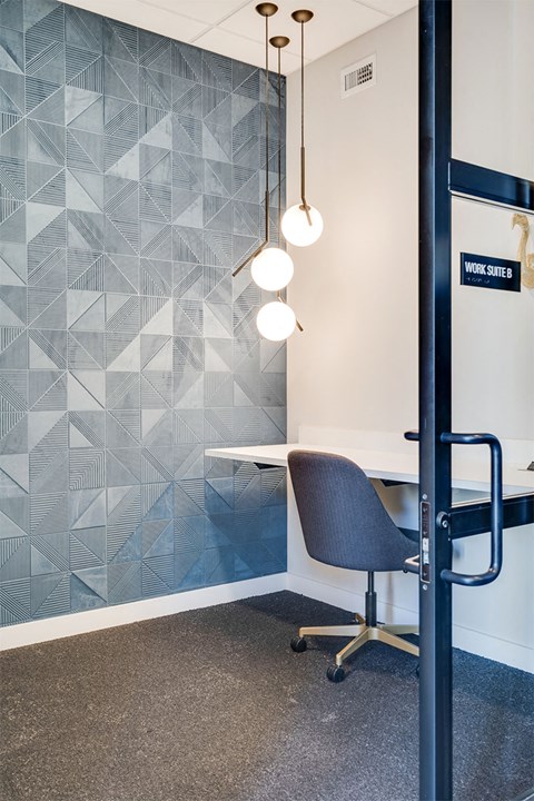A room with a grey chair and a white desk with a wallpapered wall.