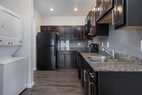 A kitchen with a black refrigerator and brown cabinets.