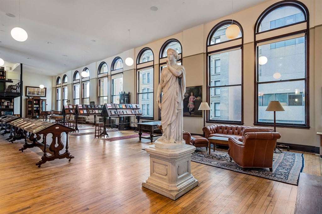 A statue of a woman stands in a room with wooden floors and a large window.