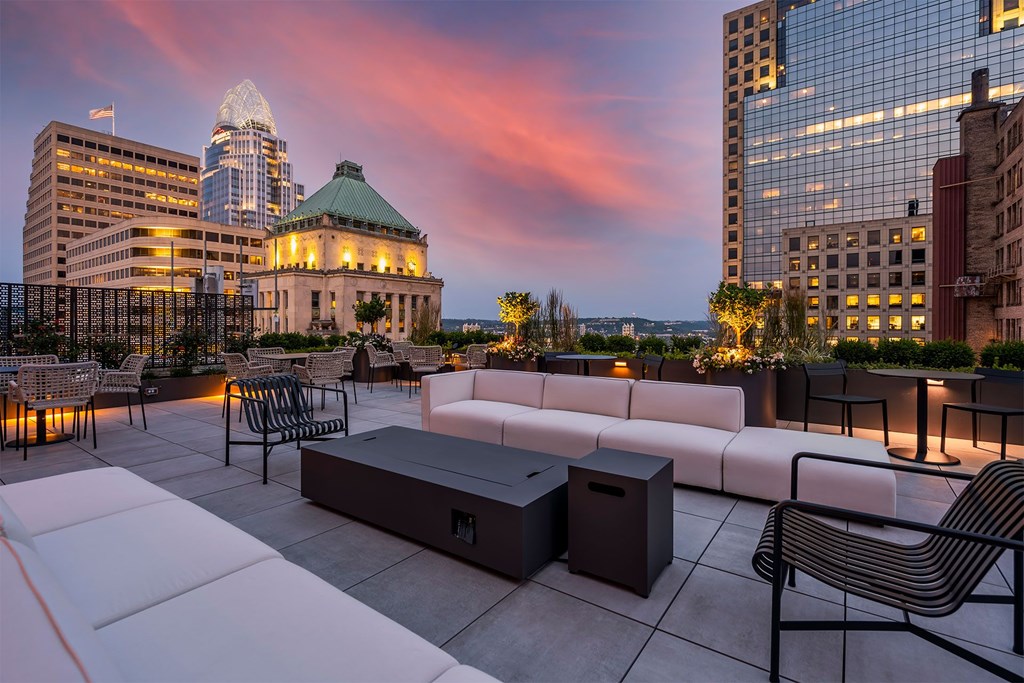 A rooftop patio with a white couch and chairs overlooking a city skyline at dusk.