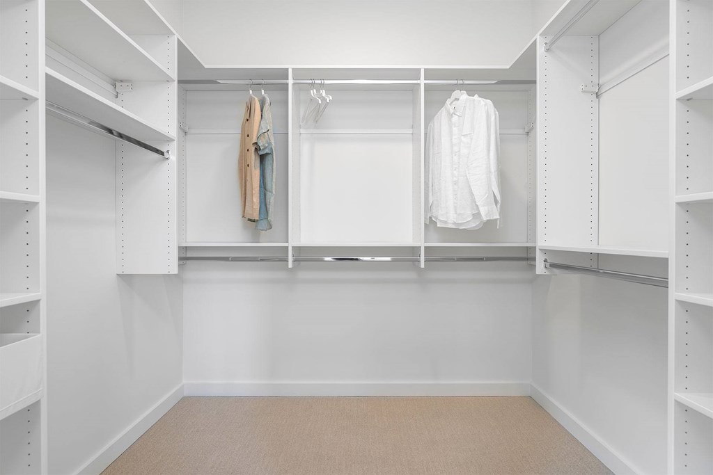 A white closet with clothes hanging on hangers.