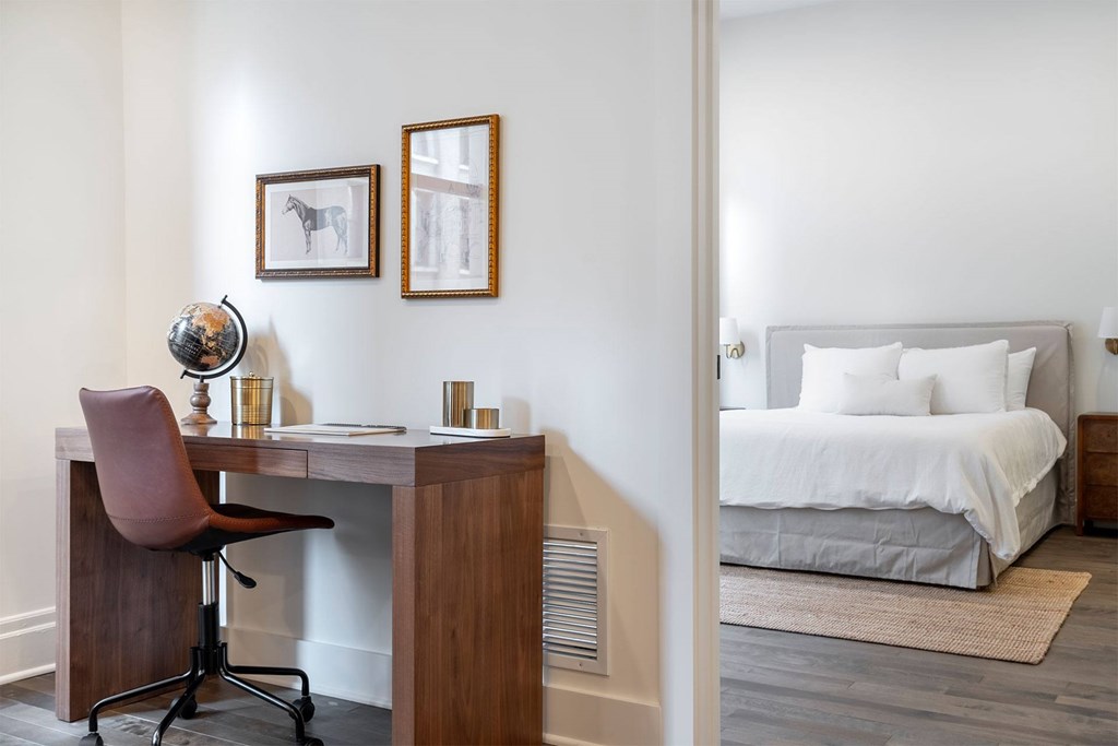 A desk with a chair and a globe on it with a bed in the background.