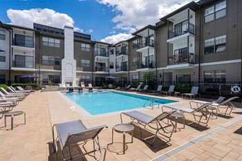 a swimming pool with tables and chairs in front of an apartment building