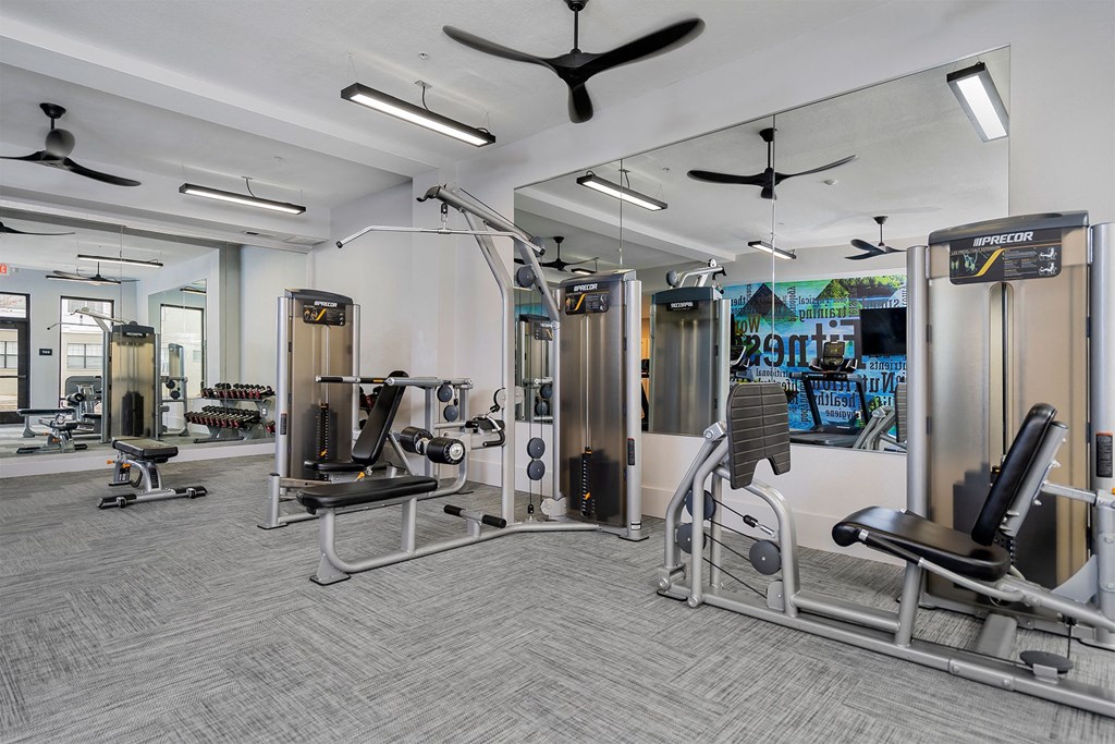 a gym with cardio equipment and weights in a building with glass walls