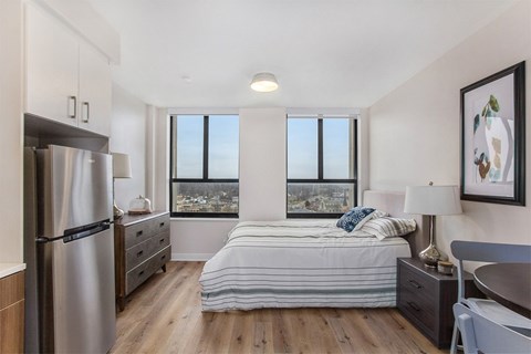 A bedroom with a bed, nightstand, and a refrigerator.