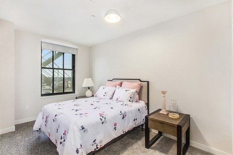 A bedroom with a bed, nightstand, and window.
