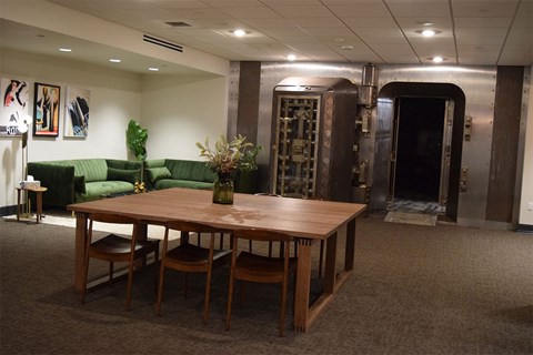 A room with a table and chairs in the foreground and a green couch in the background.
