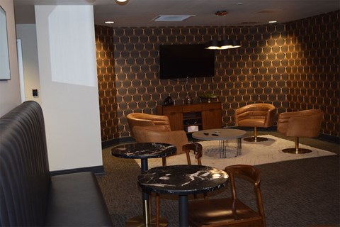 A room with a black couch, a table with a glass top, and a television mounted on the wall.