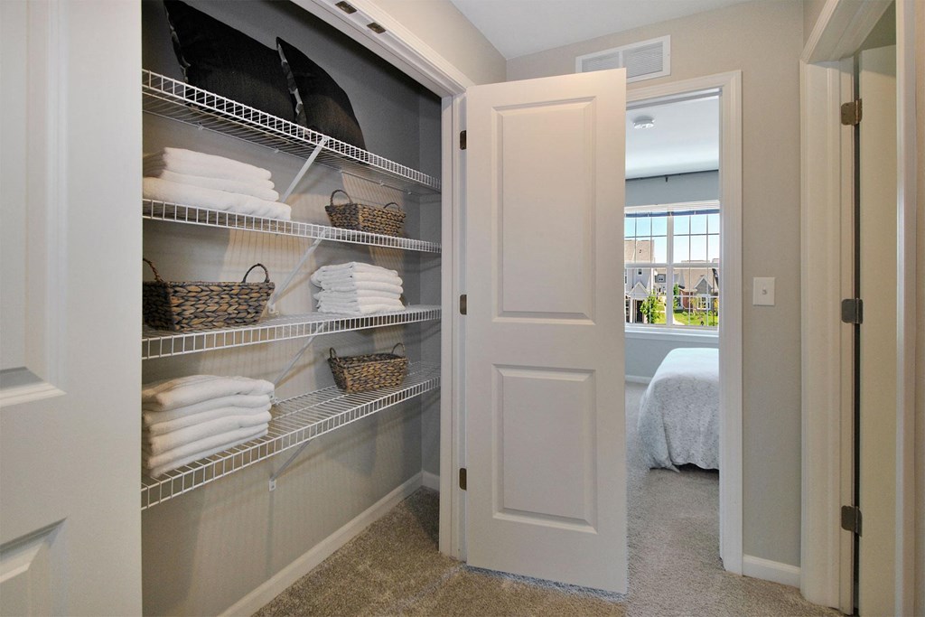 a closet with shelves and towels and a door to a bedroom