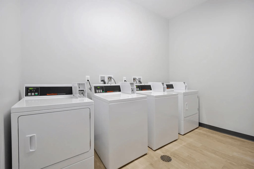 four washers and dryers in a room with white walls and wood floors