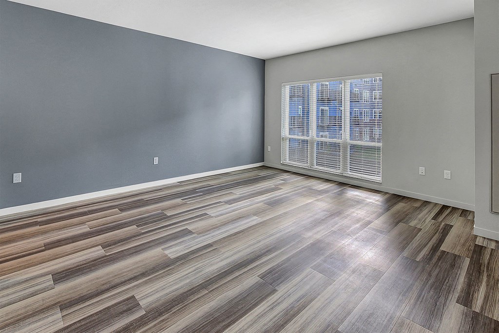 an empty living room with a large window and wooden floors