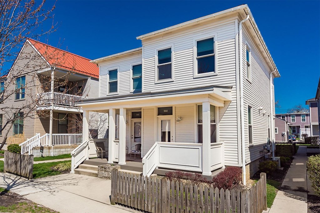 A white two-story house with a red roof and a wooden fence in front.