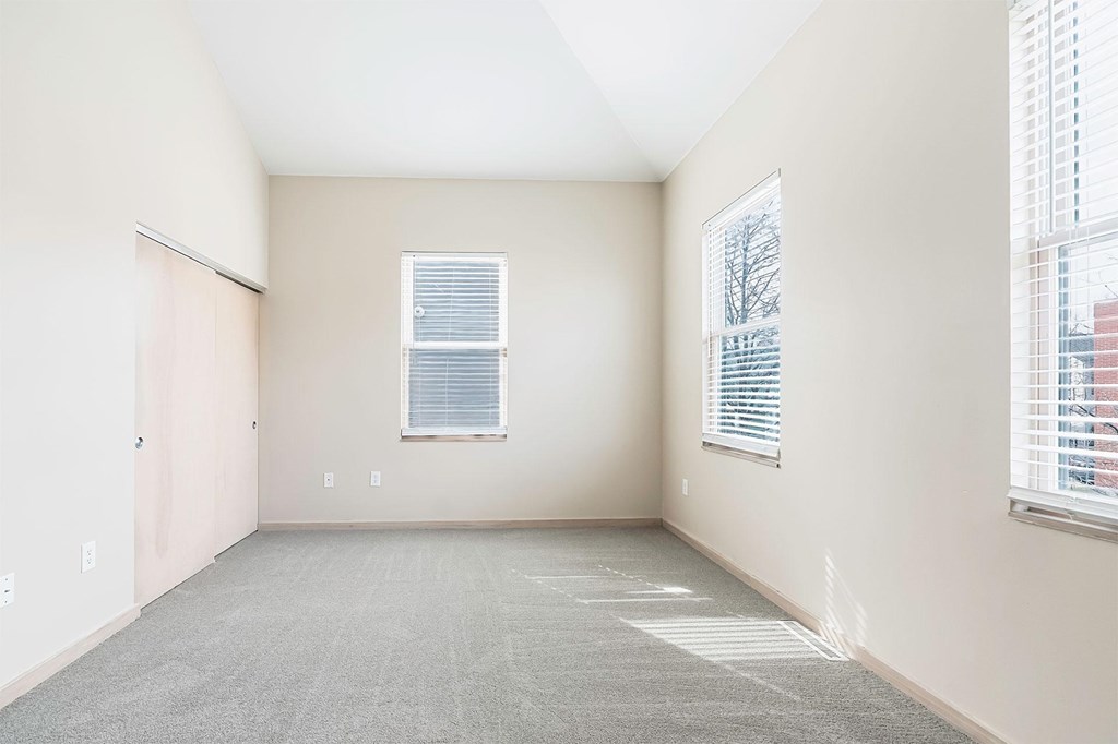 A room with a carpeted floor, a window with blinds, and a door.