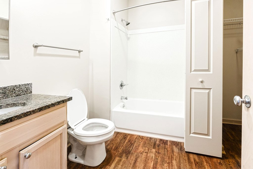 A white toilet sits in a bathroom with a wooden floor.