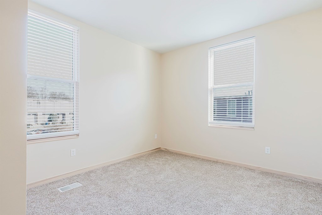 A room with a carpeted floor and two windows.
