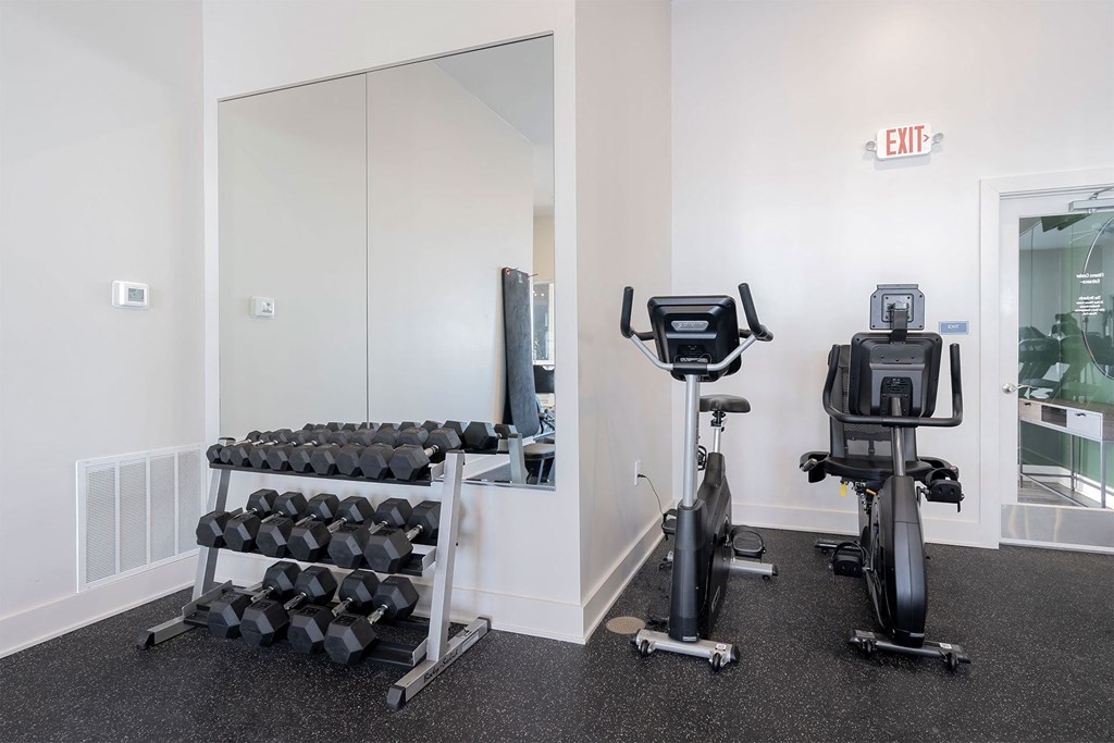 A gym room with a mirror, dumbbells, and exercise bikes.