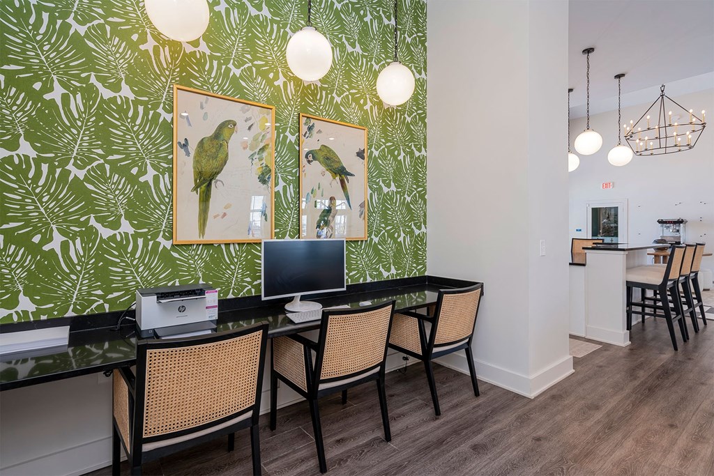 A room with a green leafy wallpaper and a desk with a computer and chairs.