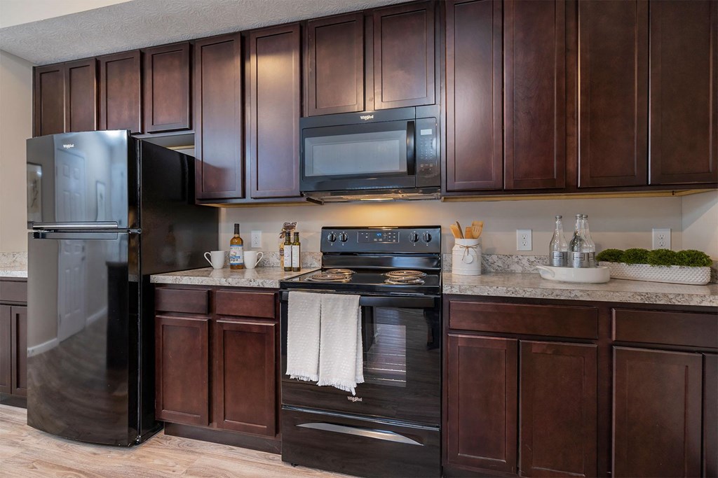 A kitchen with dark brown cabinets and a black refrigerator.
