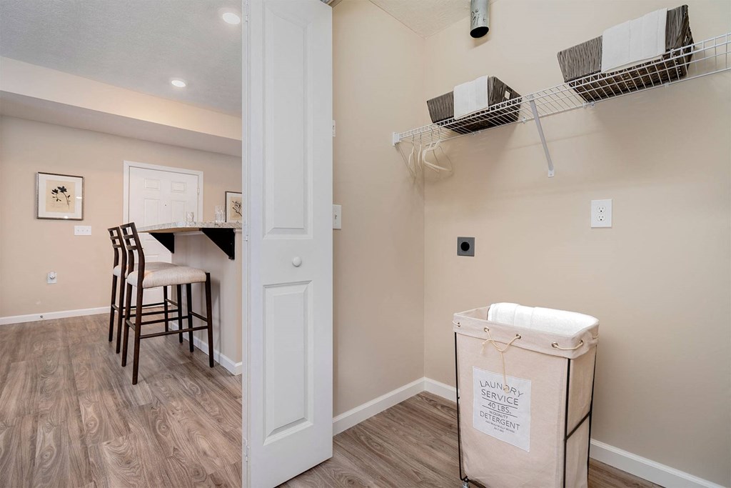 A room with a white door, a table with chairs, and a laundry basket on the floor.