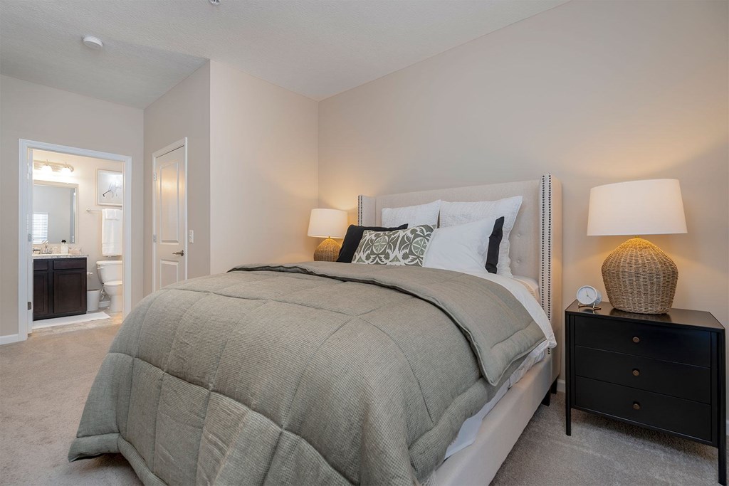 A bedroom with a large bed and a nightstand with a lamp.