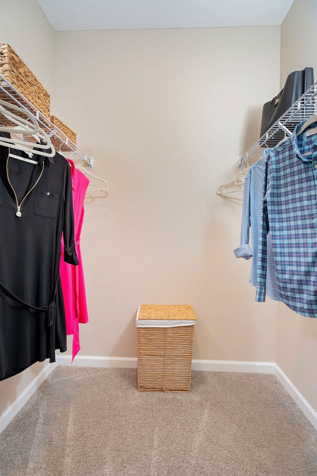 A closet with clothes hanging and a basket on the floor.