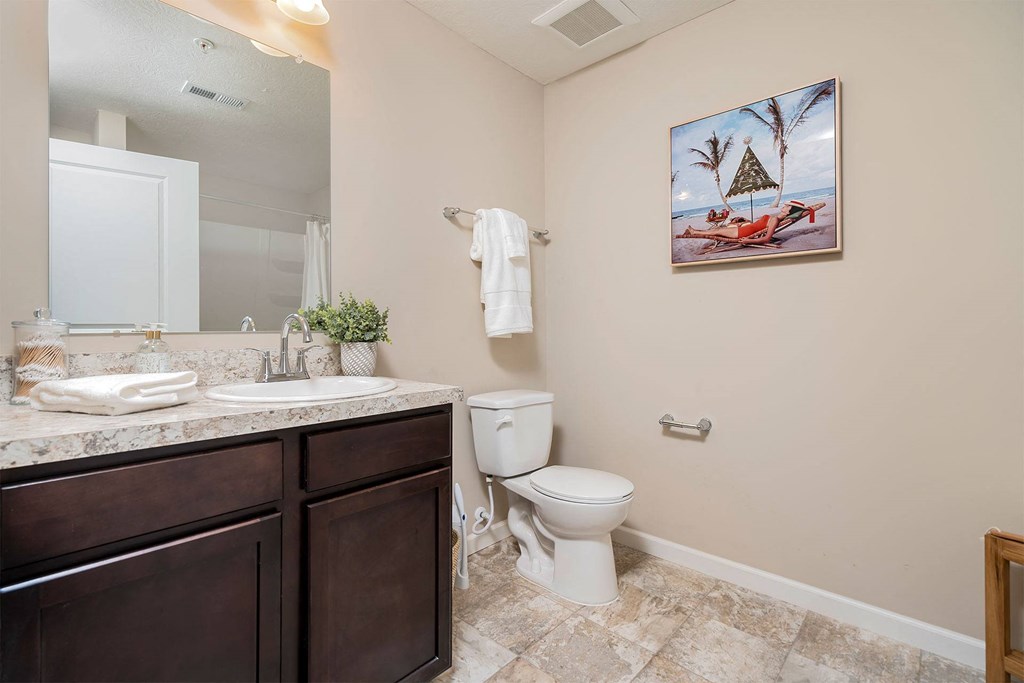 A bathroom with a toilet, sink, and a painting of a beach scene on the wall.