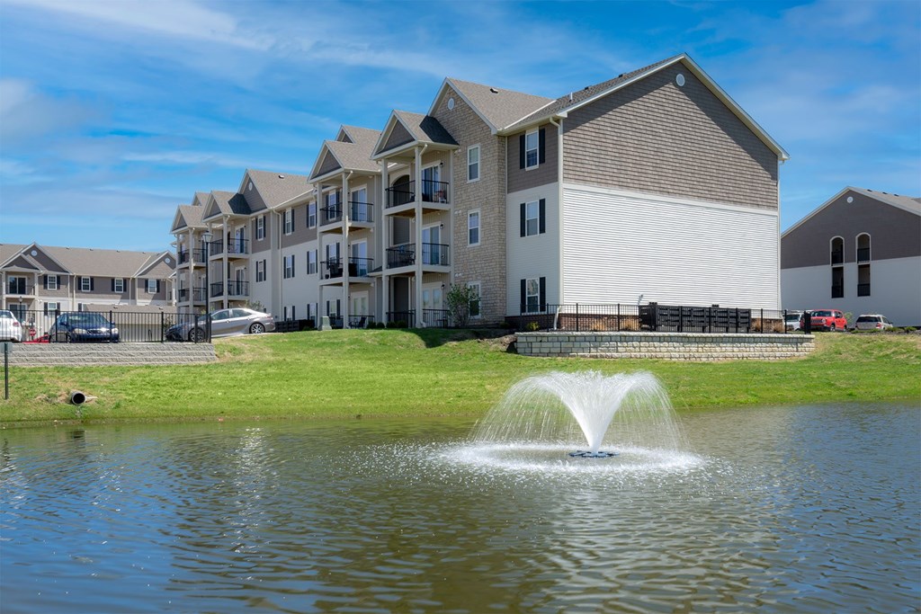 A fountain in the middle of a pond in front of a building.
