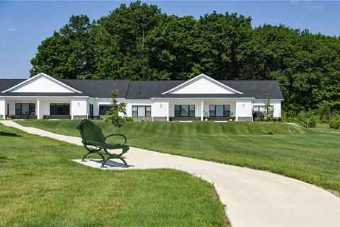 A green bench is in the foreground of a white building with a black roof.