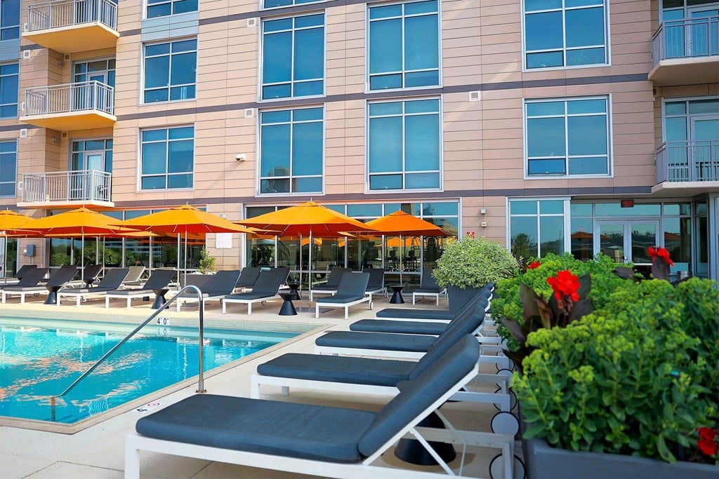 A pool area with sun loungers and umbrellas in front of a building.