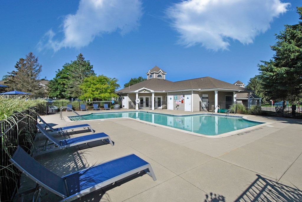 a swimming pool with blue chairs and a building in the background