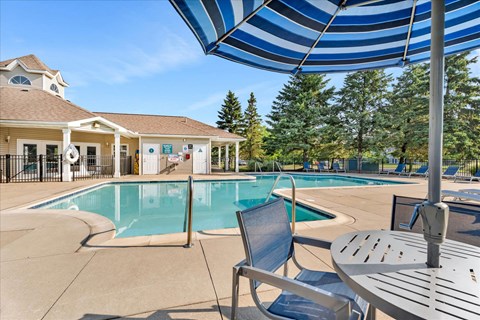 A pool area with a table and chairs under a blue and white striped umbrella.