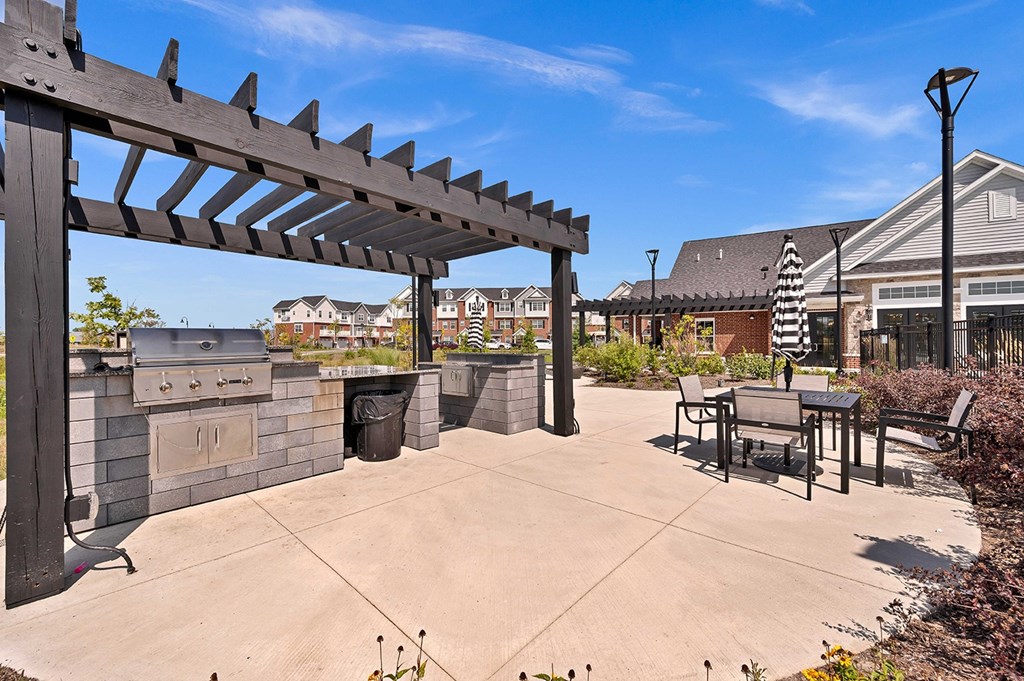 A wooden pergola is over a table and chairs in a courtyard.