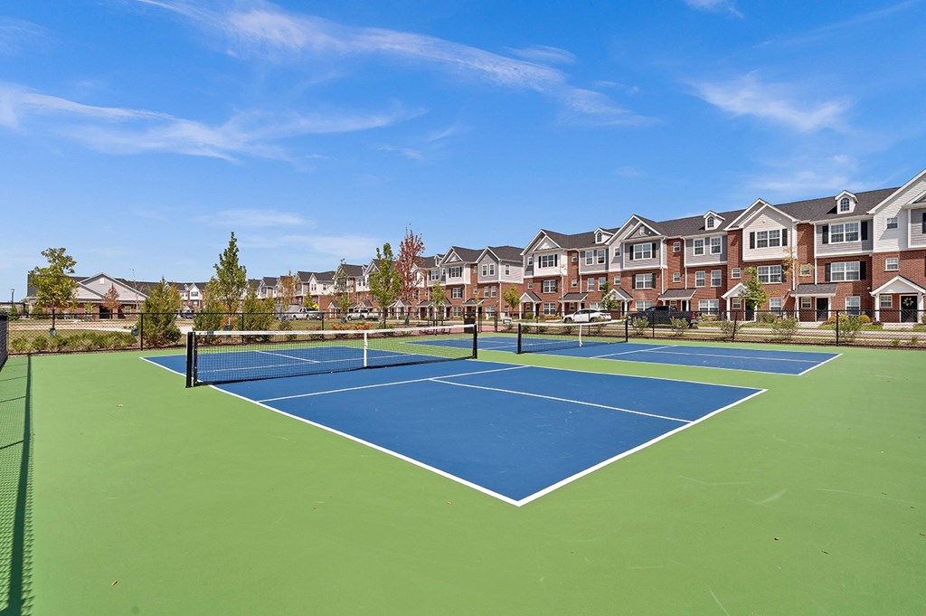 A tennis court is surrounded by apartment buildings.