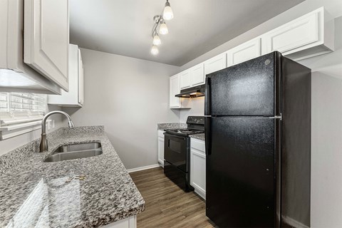 A black refrigerator stands in a kitchen with white cabinets and a granite countertop.