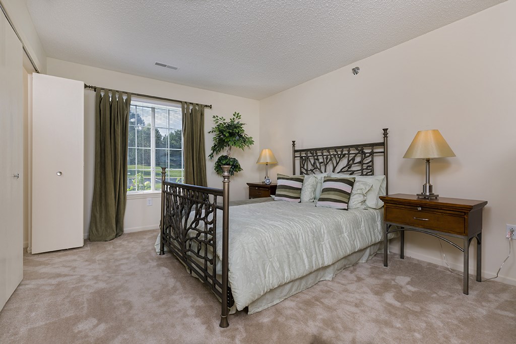 A bedroom with a bed, nightstand, and window.