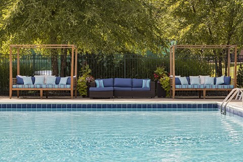 A pool with a blue tinted water and a wooden bench with white cushion.