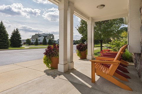 A wooden bench is on a porch with a view of a green lawn and a house.
