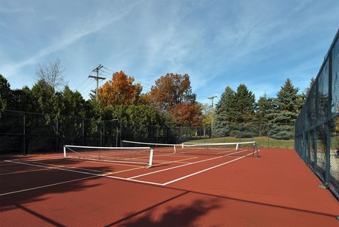 A red tennis court surrounded by trees and a fence.
