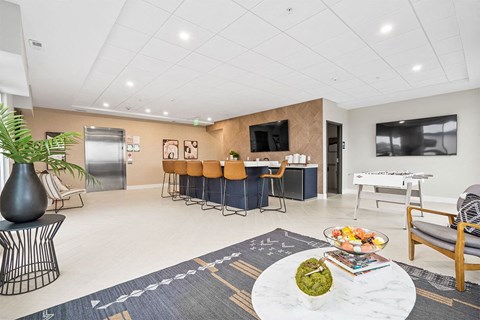 A living room with a large rug and a table with a bowl of fruit on it.