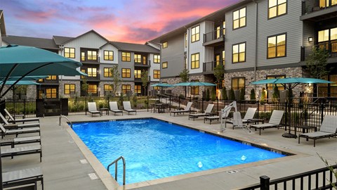 A swimming pool surrounded by lounge chairs and umbrellas in front of a building.