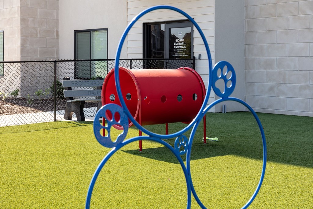 A red and blue sculpture resembling a dog is in the foreground of a grassy area.