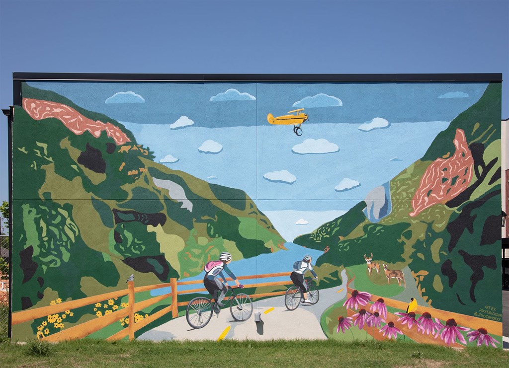 A mural depicts a cyclist and a pedestrian on a path through a mountainous landscape.