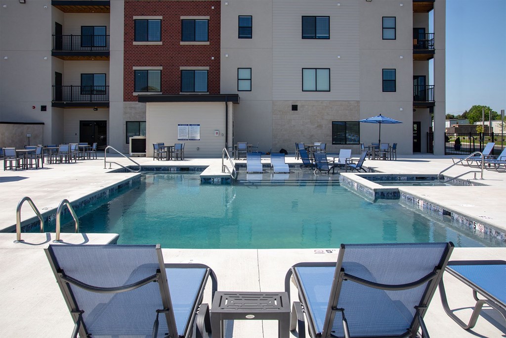 A pool surrounded by chairs and tables in front of a building.