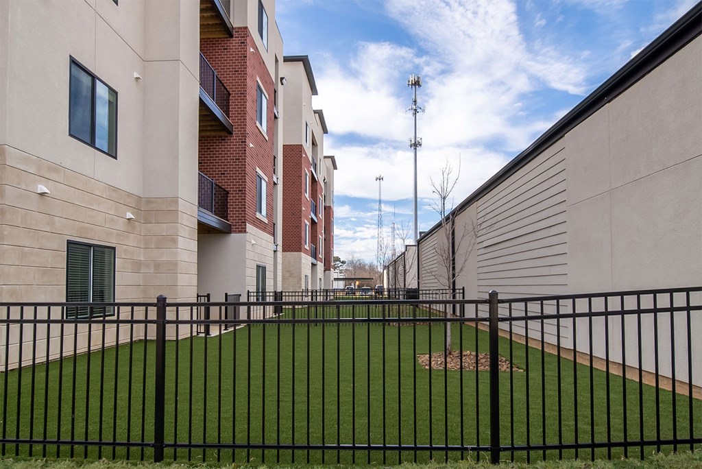 A black fence surrounds a green field in front of a building.